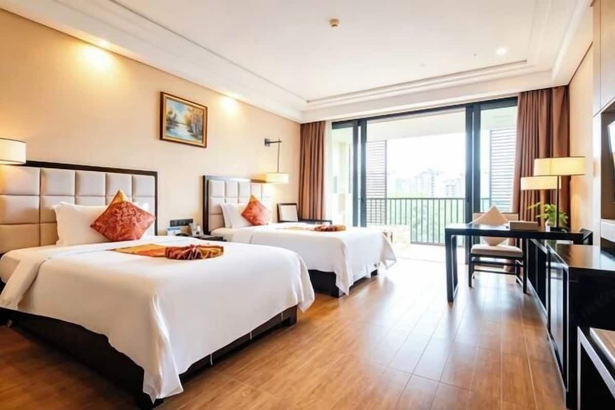 Habitación de hotel con dos camas, un escritorio y balcón con vista a la ciudad.