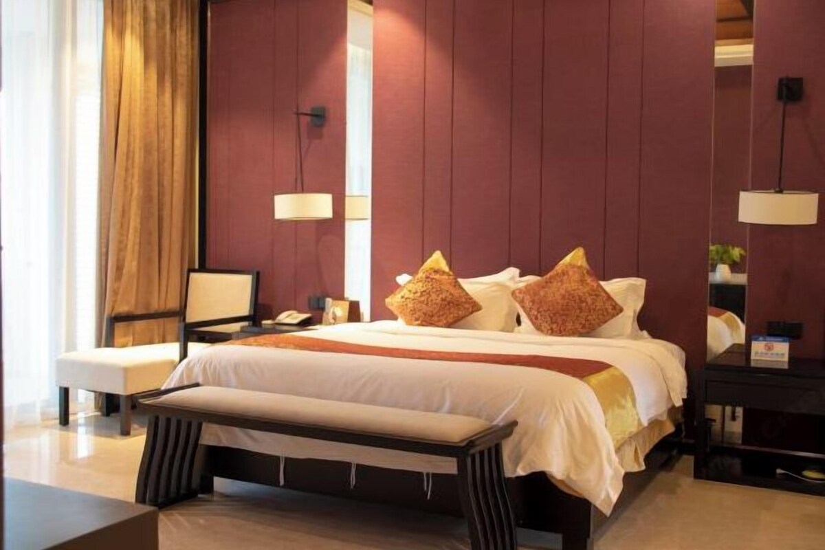 Une chambre d’hôtel avec un grand lit, une table de chevet, un banc et un miroir.