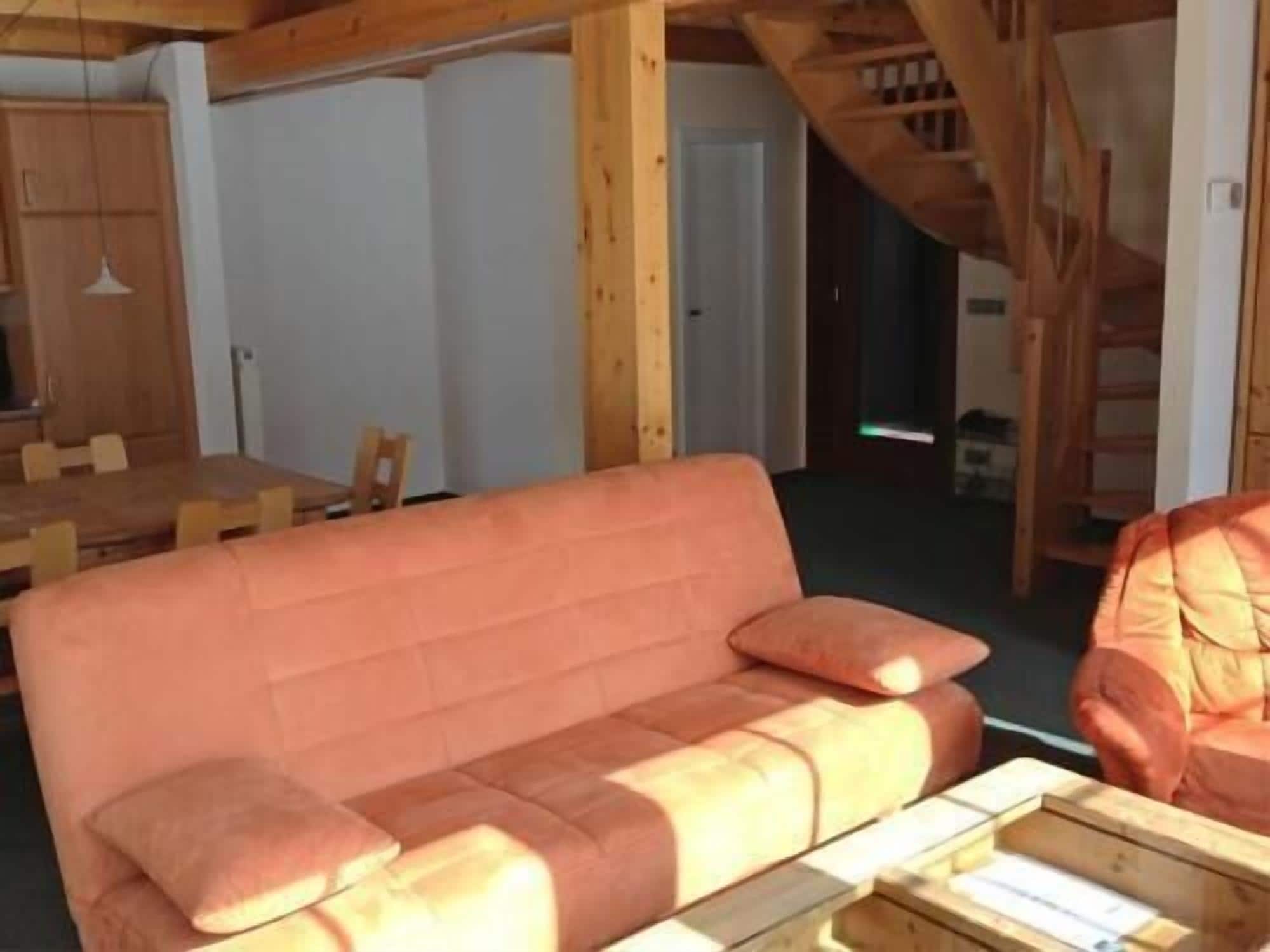 Ein Zimmer mit Holzboden, einer Couch, einem Esstisch mit Stühlen und einer Treppe.