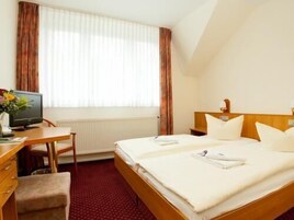 Habitación de hotel con cama, escritorio con computadora, silla y ventana con cortinas.
