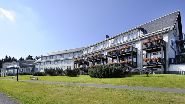 Een meerlaags hotel met balkons versierd met bloembakken, een bord waarop restaurant, café, terras en bowlinghal staan aangegeven.