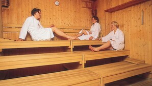 Een houten sauna met drie banken, elk bezet door een persoon in witte gewaden.