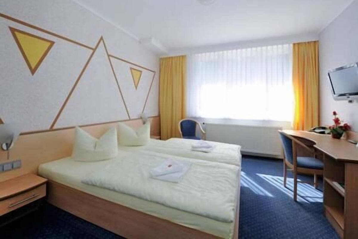 Hotellihuone, jossa on kaksi sänkyä, työpöytä, tuoli, televisio ja ikkuna, jossa on verhot.