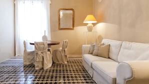 A room with a patterned floor, a white sofa, a table with chairs, a lamp, and a mirror on the wall.