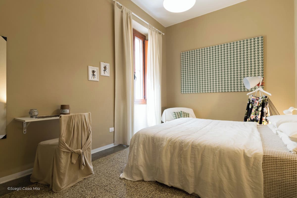 Een hotelkamer met een bed, een stoel, een kleine tafel en een wandlamp.