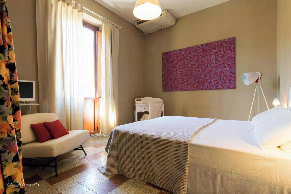 Een hotelkamer met een bed, een stoel, een bureau, een lamp en een schilderij aan de muur.