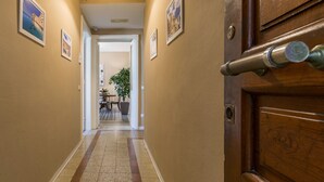 A hallway with framed pictures on the walls, a wooden door with a handle, and a tiled floor.