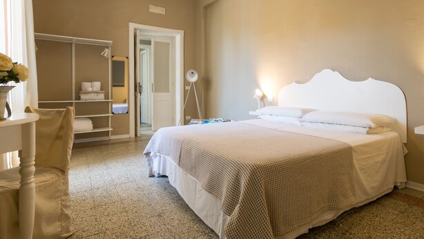 A bedroom with a large bed, a bedside table, a chair, a wardrobe, and a mirror.