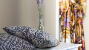 A bed with two patterned pillows, a vase with flowers, and a colorful curtain in the background.