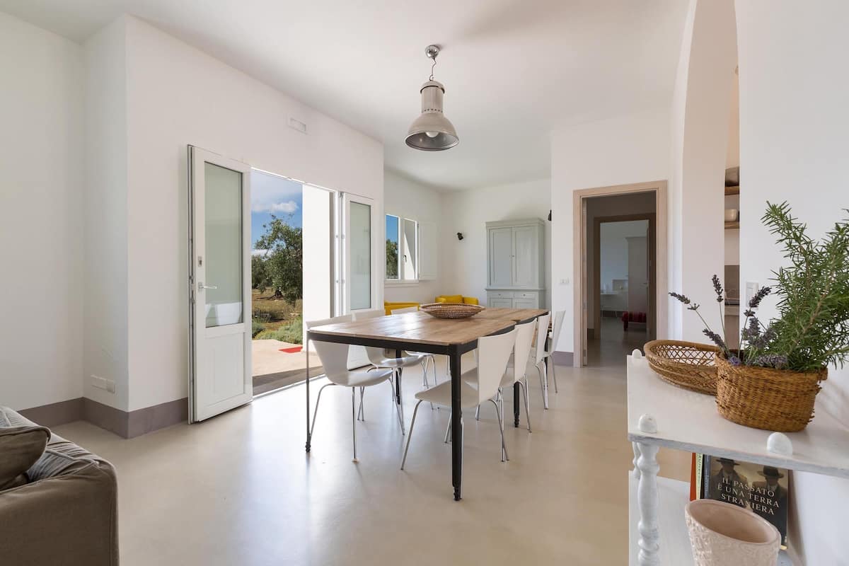 A modern kitchen with a wooden table, white chairs, and a hanging light fixture.