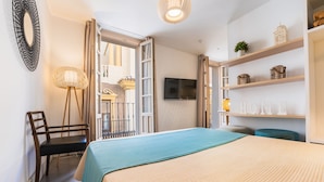 Une chambre à coucher comprenant un lit, une chaise, un téléviseur et des étagères ornées d’objets décoratifs.