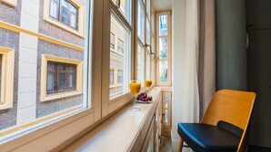 Une pièce avec une fenêtre, une chaise et une table sur laquelle se trouvent deux verres de jus d’orange et une assiette de raisins.
