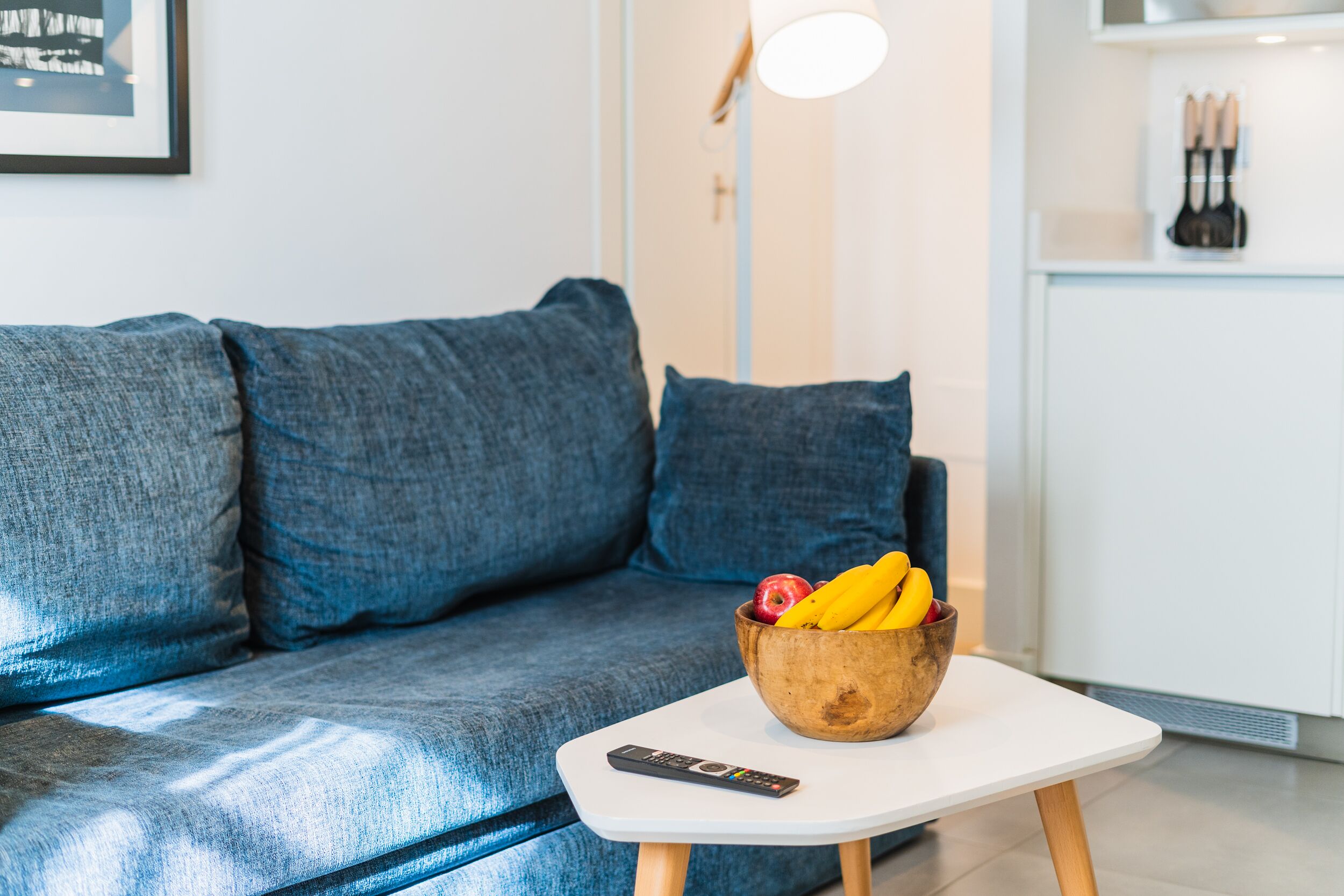 Een moderne woonkamer met een grijze bank, een klein wit tafeltje en een houten schaal met fruit.