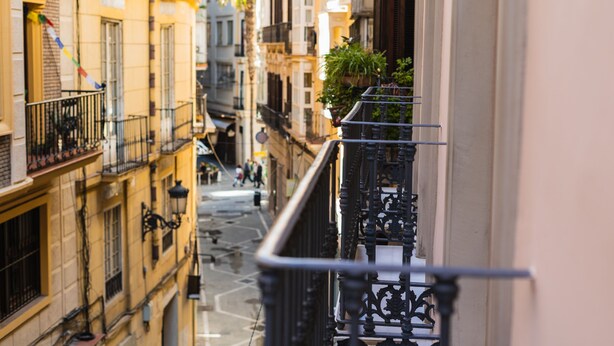 Une rue étroite, bordée de bâtiments des deux côtés, avec des balcons dotés de garde-corps et des fenêtres.