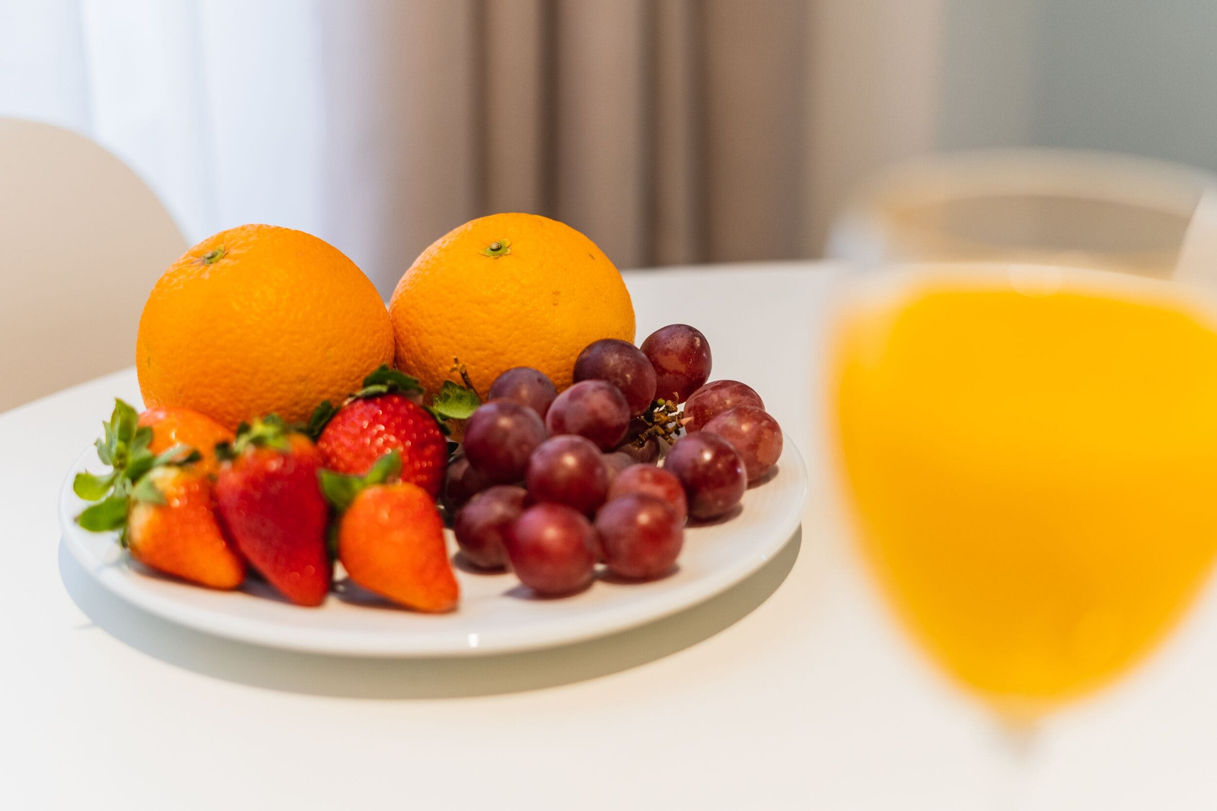 A plate with oranges, strawberries, and grapes on a white table.