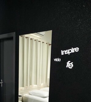 A hotel room with a bed, curtains, and a wall with the words "inspire vida fe". - Hotel Barril (Primavera do Leste)