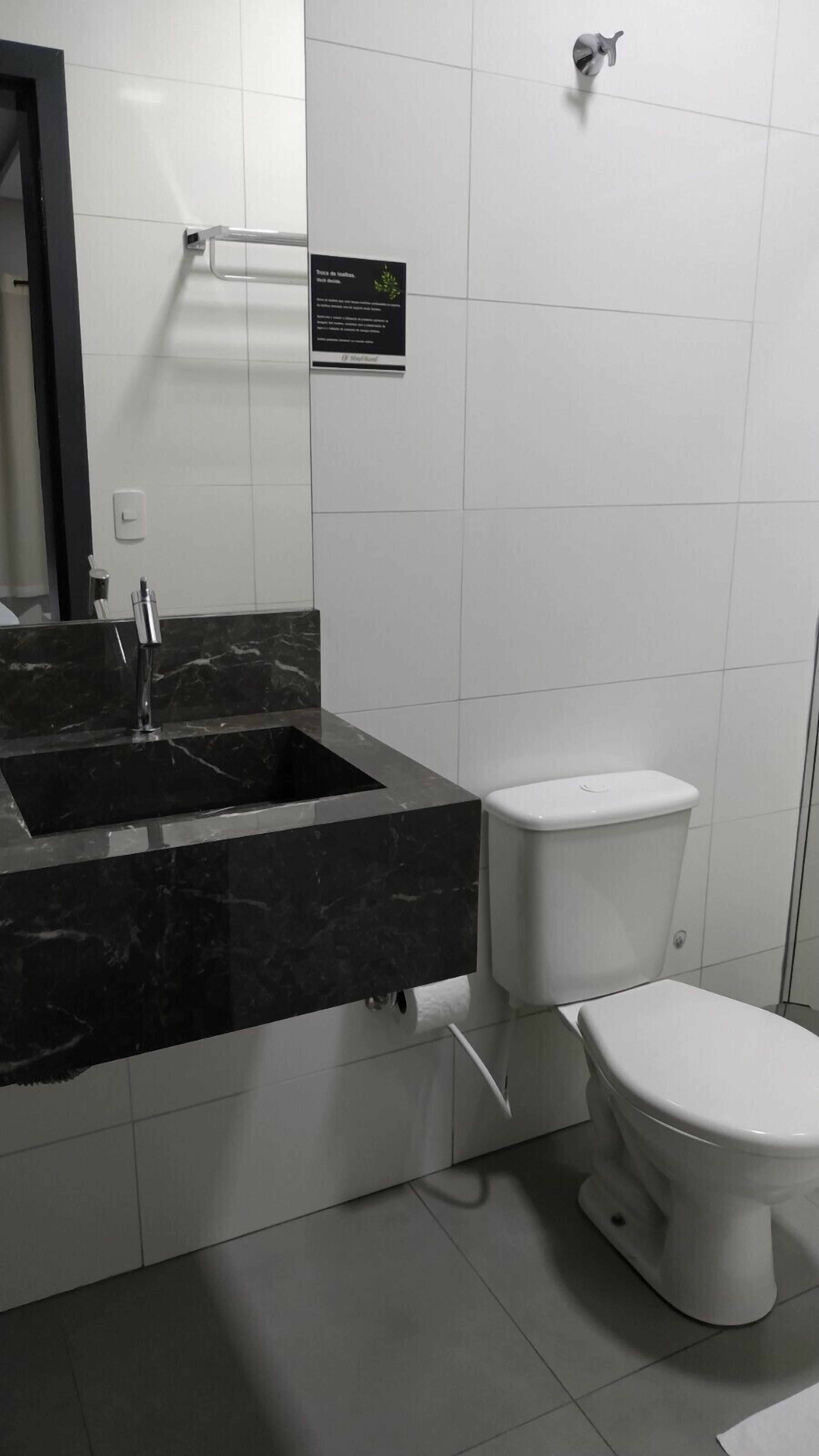 A modern bathroom with a black marble sink, white toilet, and a hand dryer.