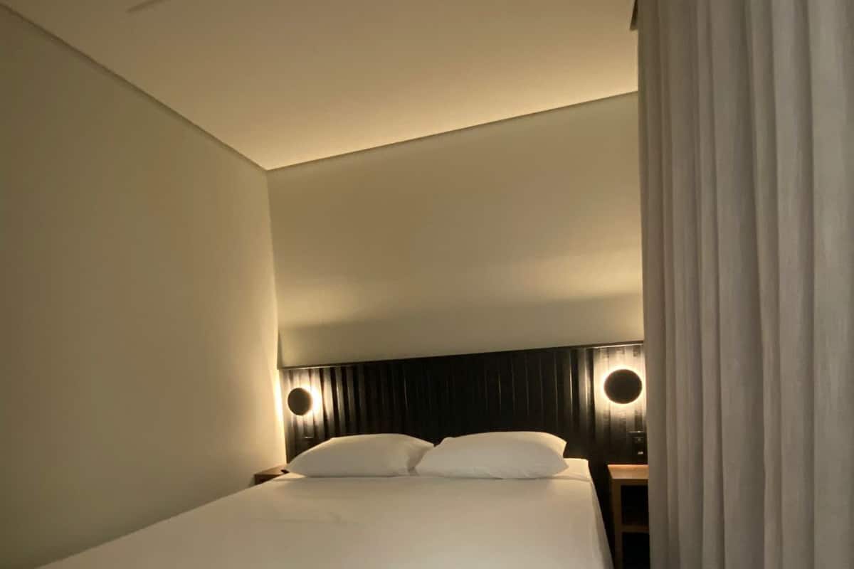 Habitación de hotel con una cama grande, dos mesitas de noche con lámparas y una cortina en la ventana.
