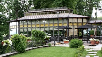Un bâtiment doté d’une grande façade vitrée, d’une terrasse avec des parasols et d’un jardin bien entretenu.