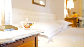Una habitación de hotel con una cama, una mesita de noche con un recipiente de vidrio, un cuadro en la pared y una lámpara en una mesita auxiliar.