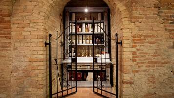 Un arco de ladrillo da paso a un espacio con estantes llenos de libros y botellas.