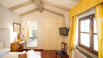 Una habitación de hotel con cama, cómoda de madera, silla, televisor y armario.