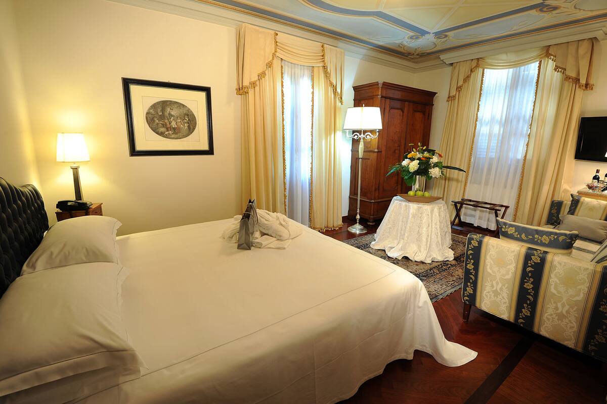 A hotel room with a large bed, a desk, a chair, a TV, and a vase with flowers.