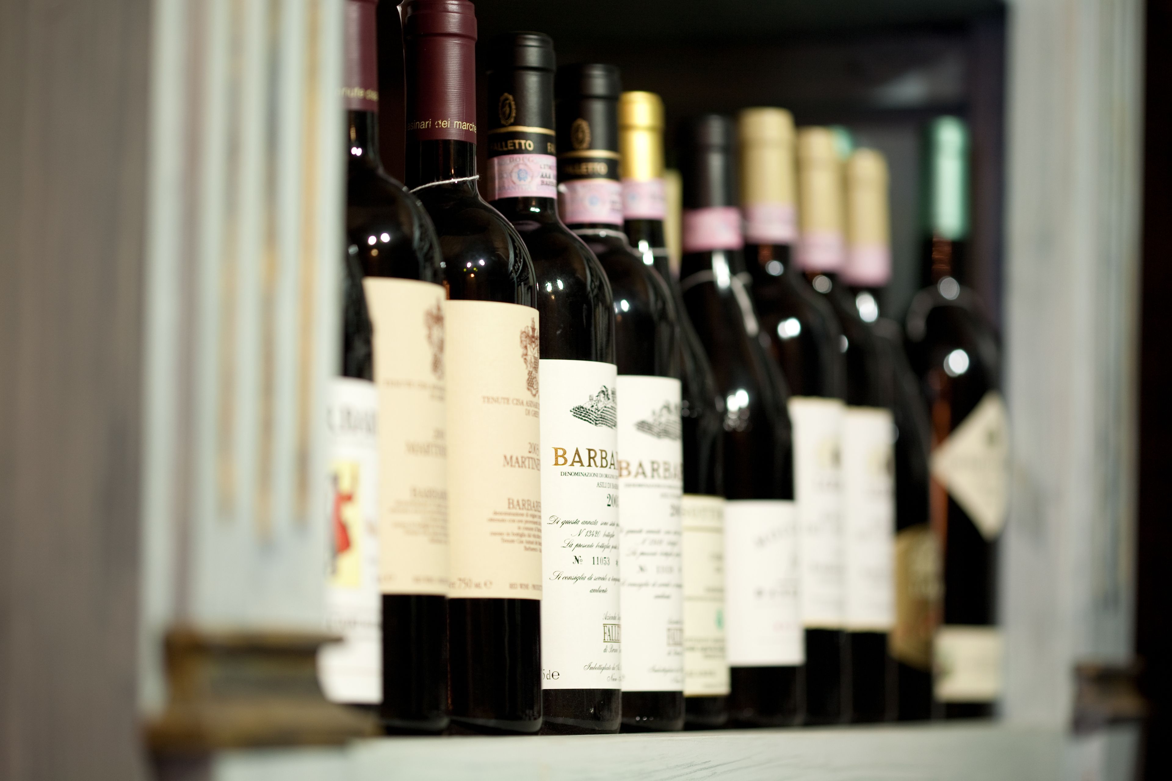 Una hilera de botellas de vino con etiquetas, probablemente en una cava o zona de almacenamiento.
