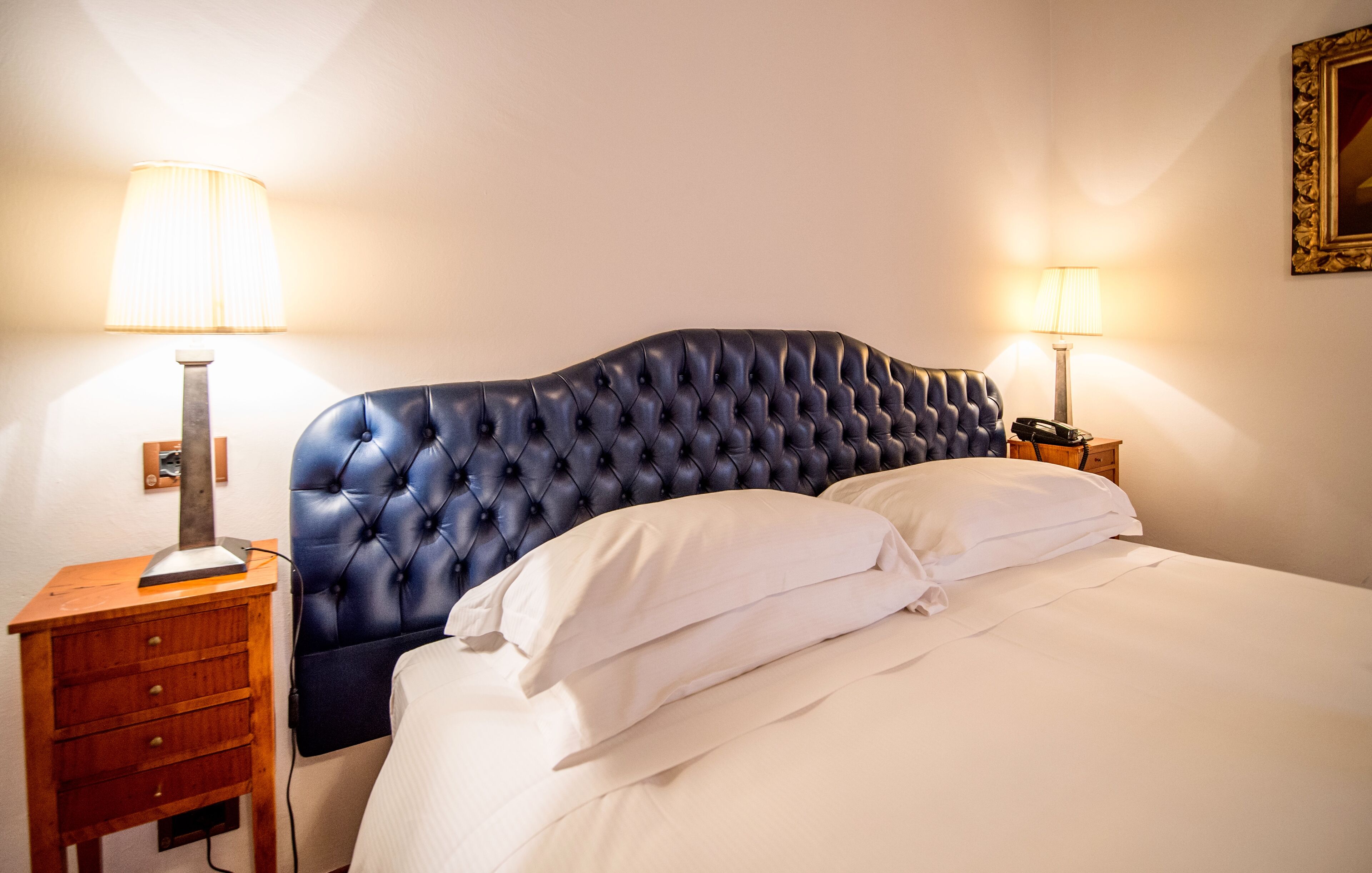 A bedroom with a tufted headboard, a wooden nightstand with drawers, a bedside table, and two lamps.