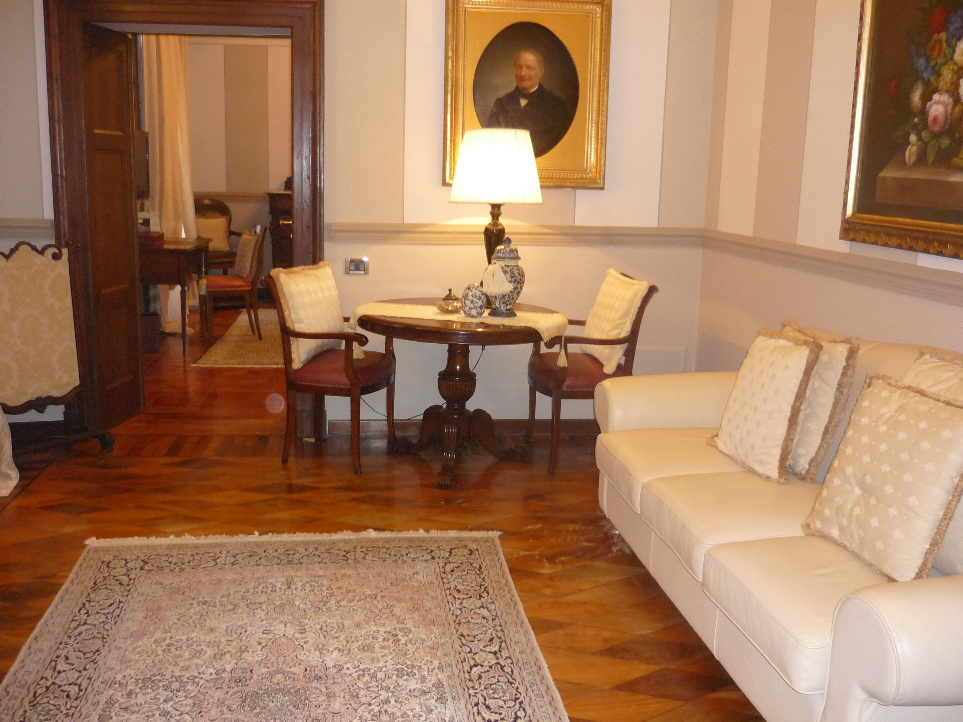 A room with a round wooden table, two chairs, a white sofa, and a patterned rug.