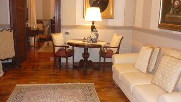 A room with a round wooden table, two chairs, a white sofa, and a patterned rug.