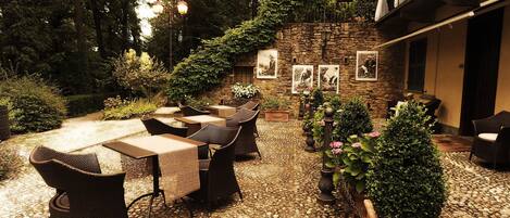 An outdoor patio with stone flooring, wicker furniture, and a stone wall with framed pictures.