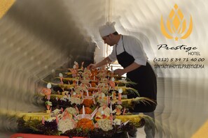 Un chef preparando comida en una cocina, con el logotipo y la información de contacto del Hotel Prestige.