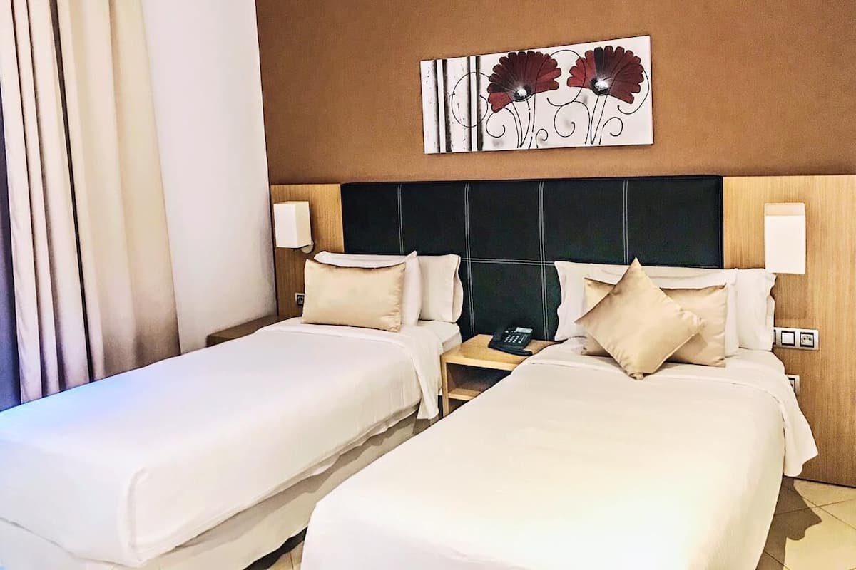 A hotel room with two beds, a headboard, bedside tables, a phone, and a wall art piece.