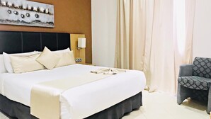 A hotel room with a large bed, a headboard, a wall-mounted artwork, a chair, and a window with curtains. - Prestige Hotel (Tetouan)