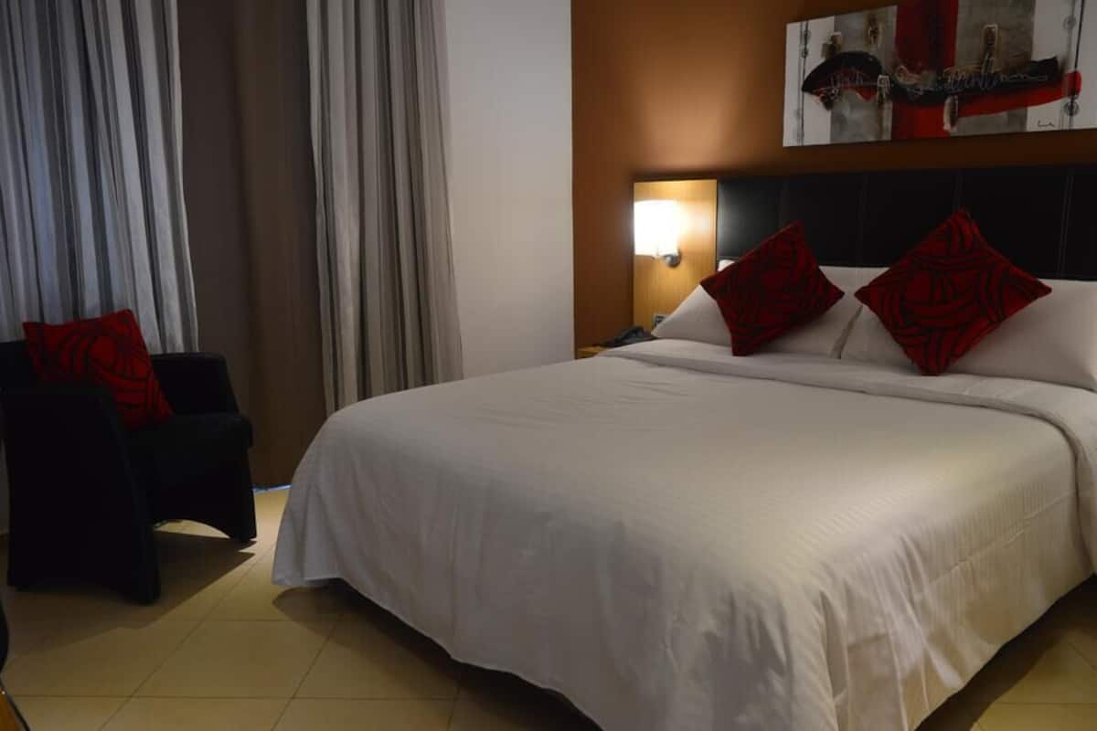A hotel room with a large bed, a bedside table, a chair, and a wall-mounted lamp.