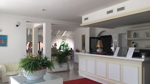 A modern living room with a white sofa, a glass coffee table, and a red rug. There is a kitchen area with a white countertop and a red lamp. - Hotel La Settima Luna (Umag)
