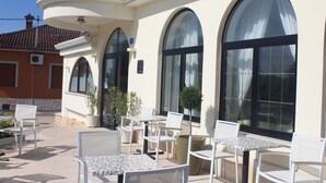An outdoor patio with white tables and chairs, large arched windows, and potted plants. - Hotel La Settima Luna (Umag)