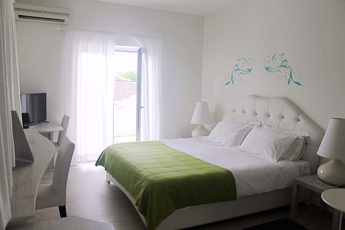 Ein Hotelzimmer mit Bett, zwei Nachttischlampen, einem Schreibtisch mit Fernseher und einem Fenster mit Vorhängen.