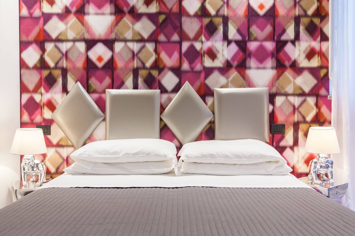 Una habitación de hotel con una cama, dos mesitas de noche y un papel tapiz estampado.