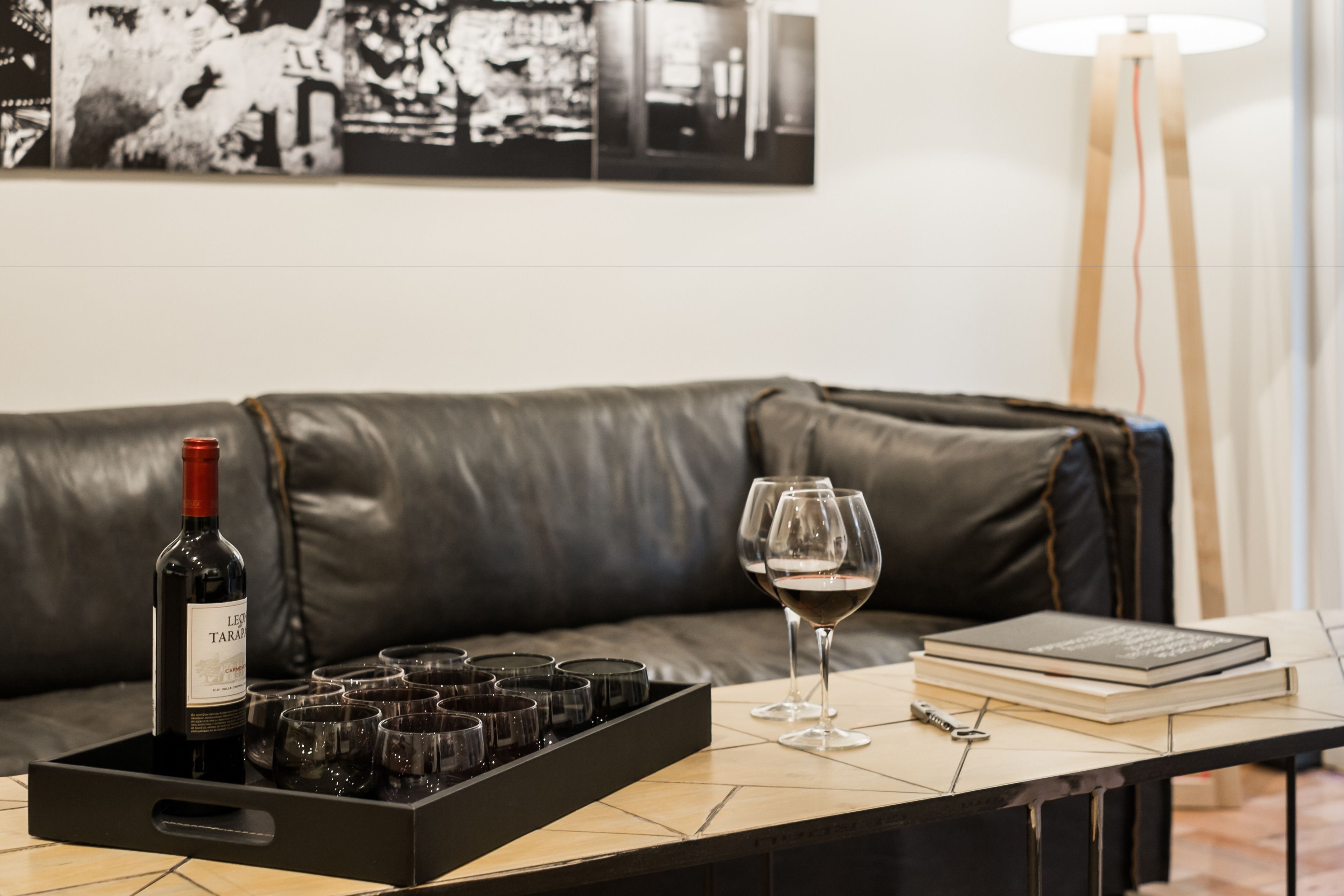 Une pièce avec un canapé en cuir, un plateau contenant des bouteilles de vin et des verres, un livre et une lampe sur pied.