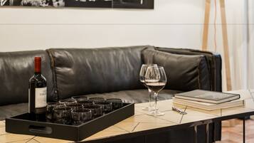 Une pièce avec un canapé en cuir, un plateau contenant des bouteilles de vin et des verres, un livre et une lampe sur pied.