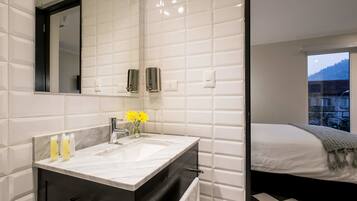 A modern bathroom with a large mirror, white tiled walls, a marble sink, and a small vase with yellow flowers.