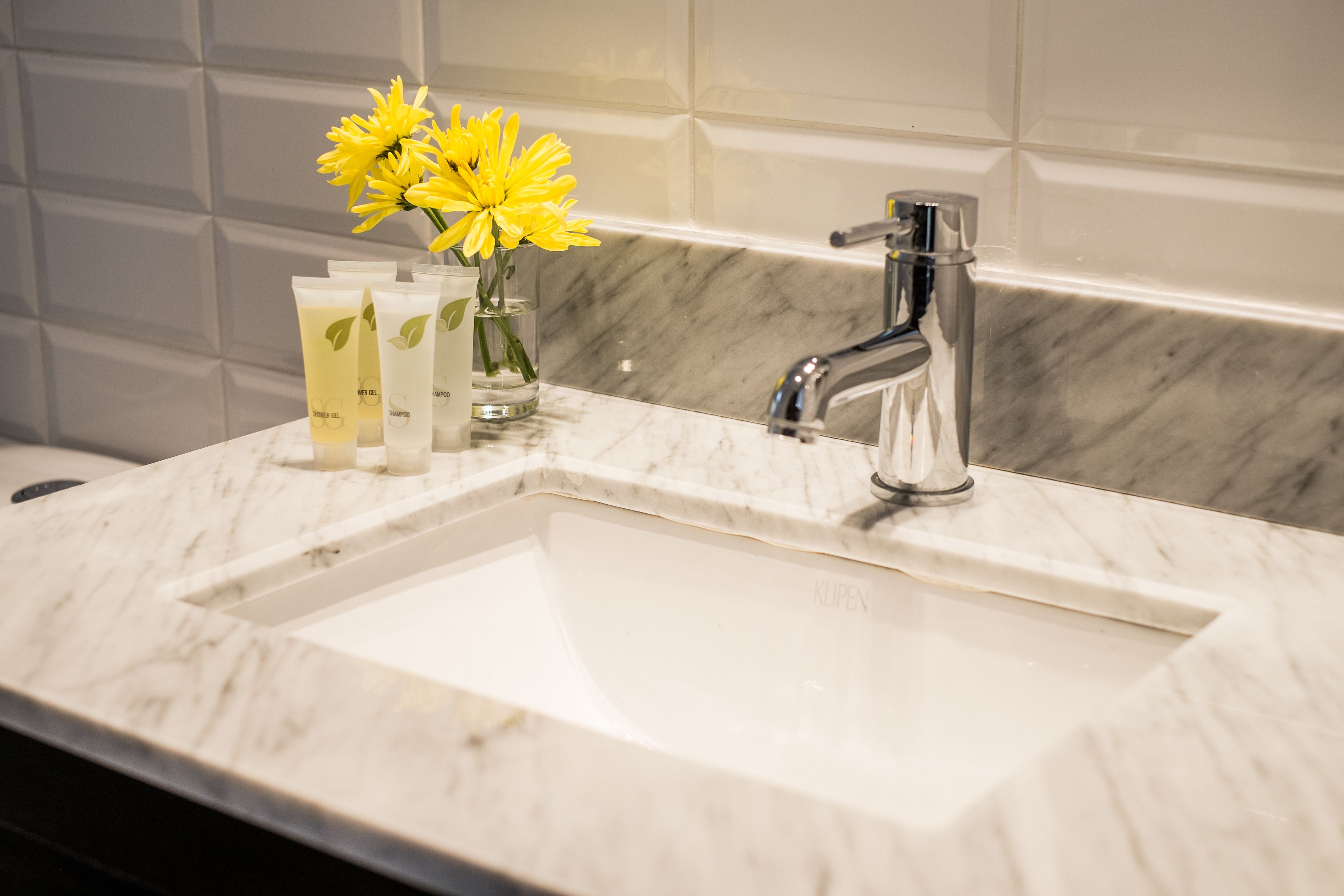 A bathroom sink with a marble countertop, a modern faucet, and a vase with yellow flowers.