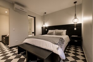 A modern bedroom with a black and white checkered floor, a large bed with a grey blanket, two bedside tables, and a hanging light fixture. - Apart Hotel B (Santiago)