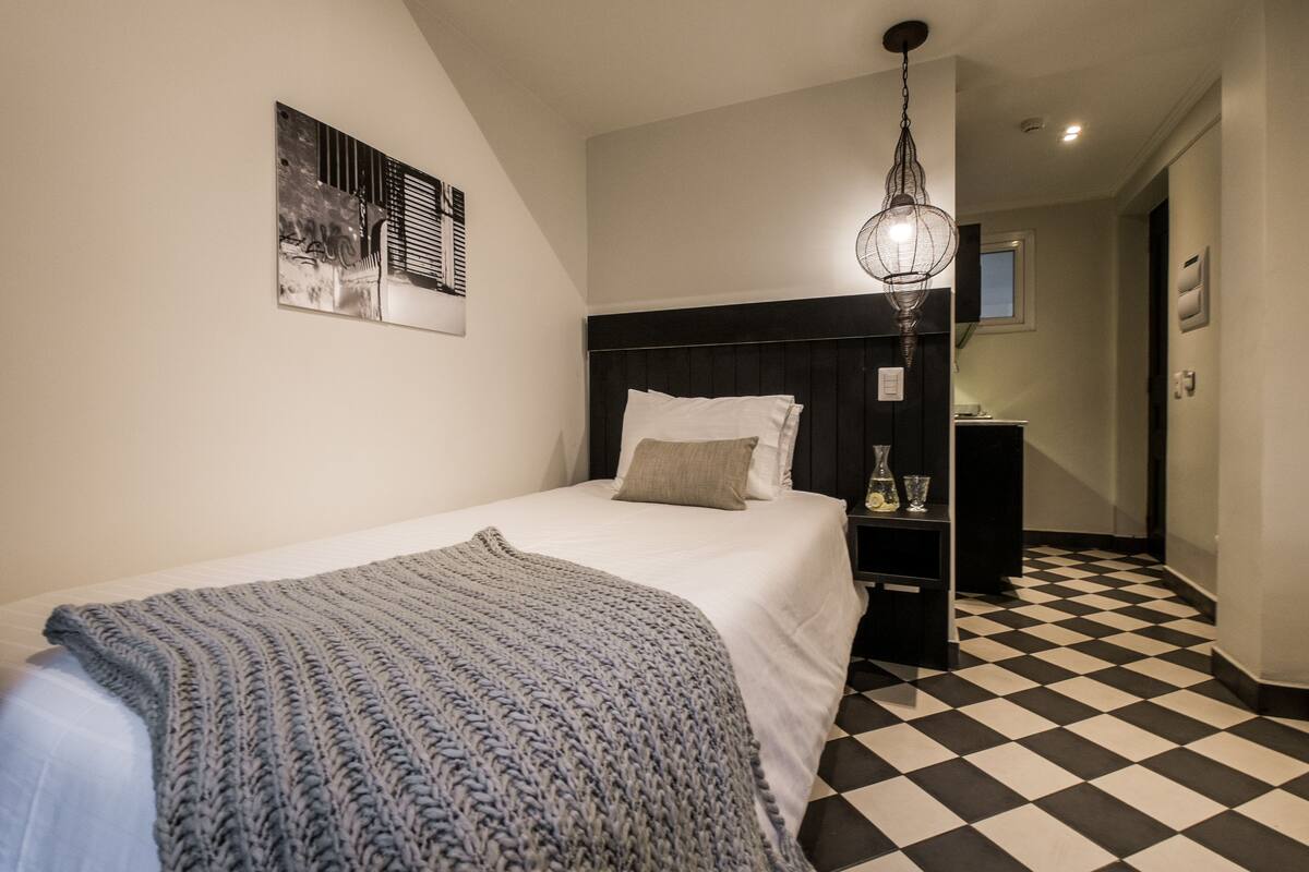 A bedroom with a bed, a nightstand, a lamp, and a checkered floor.