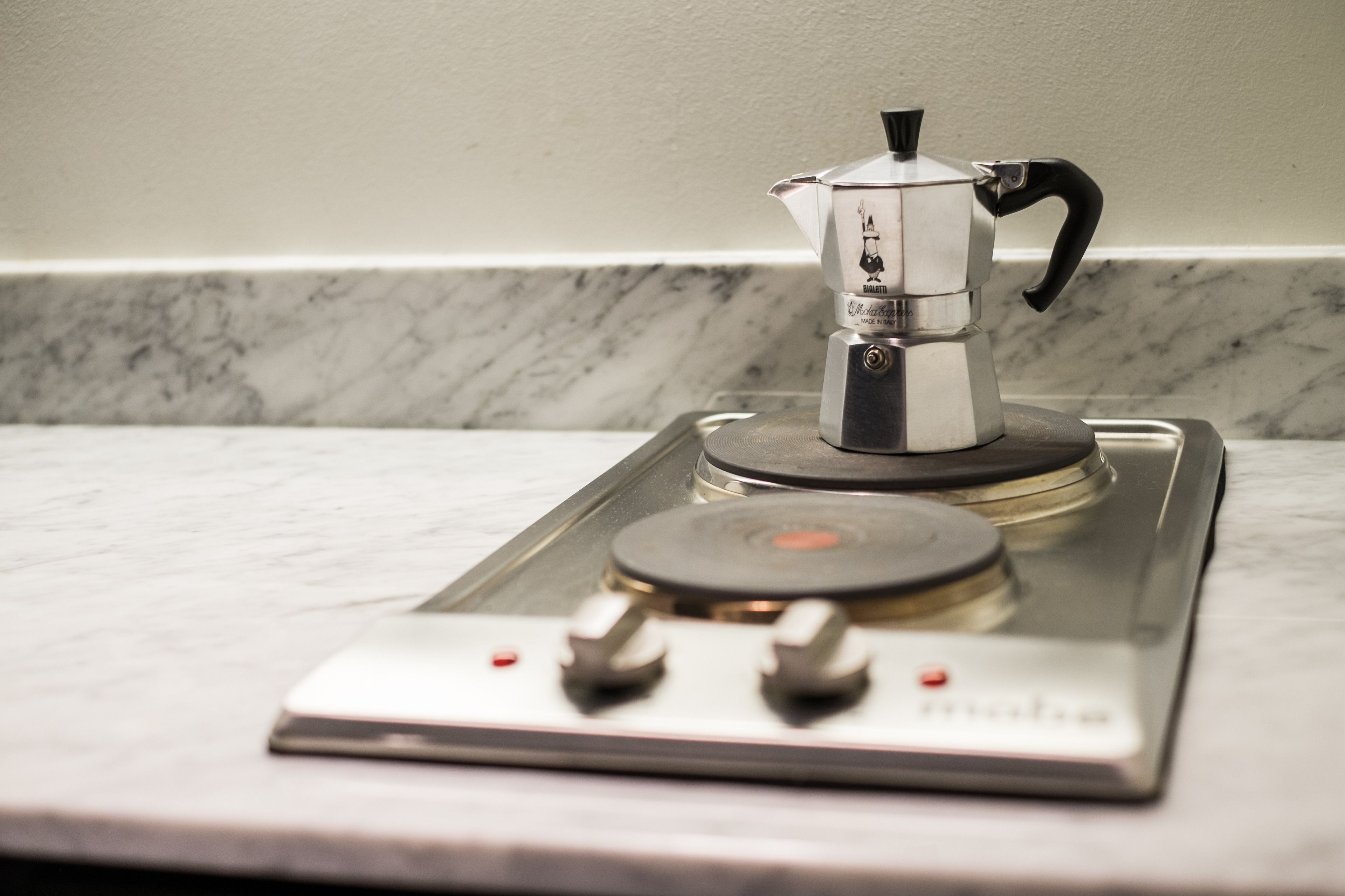 A stovetop espresso maker on a kitchen counter with a marble backsplash.