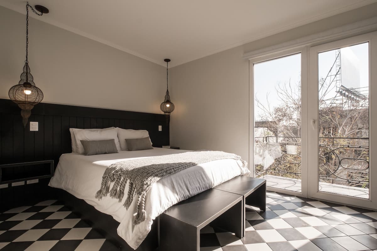 A modern bedroom with a large bed, a bench, and two hanging light fixtures.
