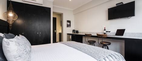 Habitación de hotel moderna con una cama grande, un escritorio con una computadora portátil, un televisor montado en la pared y una lámpara colgante.