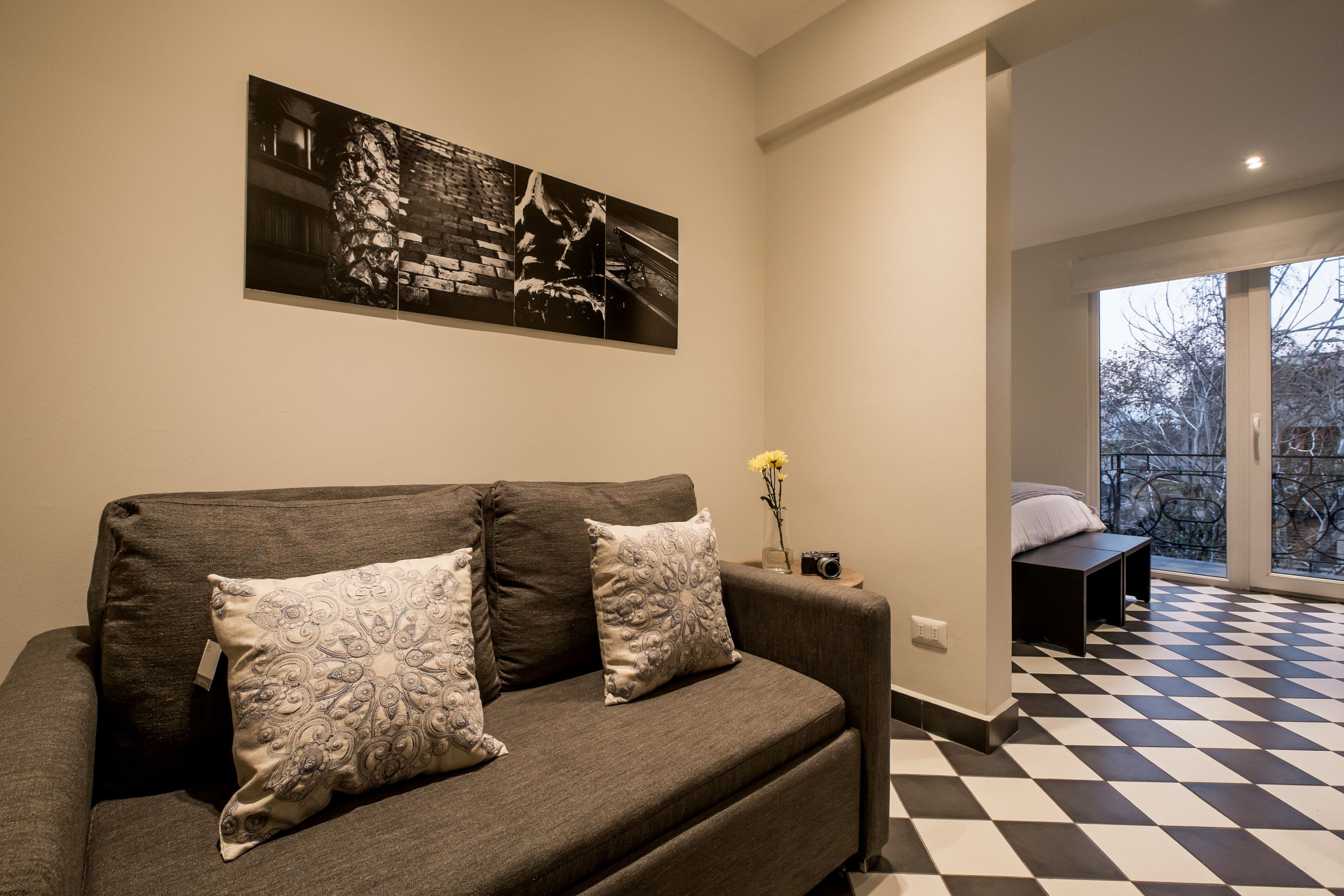 Una sala moderna con un sofá, dos cojines decorativos, una fotografía en blanco y negro enmarcada en la pared y un piso a cuadros.